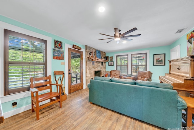 living room with light wood finished floors, a stone fireplace, visible vents, a ceiling fan, and baseboards