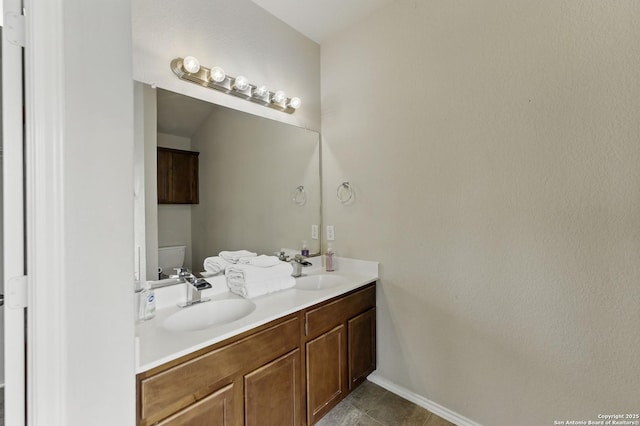bathroom with toilet, a sink, double vanity, and baseboards