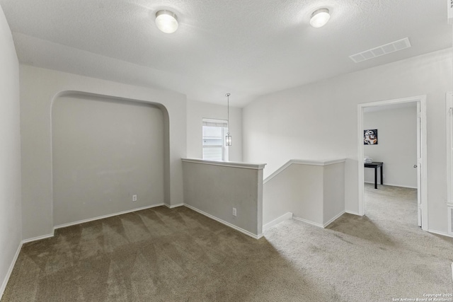 unfurnished room with visible vents, baseboards, carpet flooring, and a textured ceiling