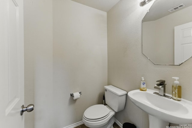 half bath with visible vents, toilet, and a sink