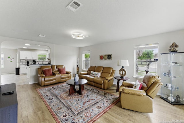 living area featuring arched walkways, light wood finished floors, and visible vents