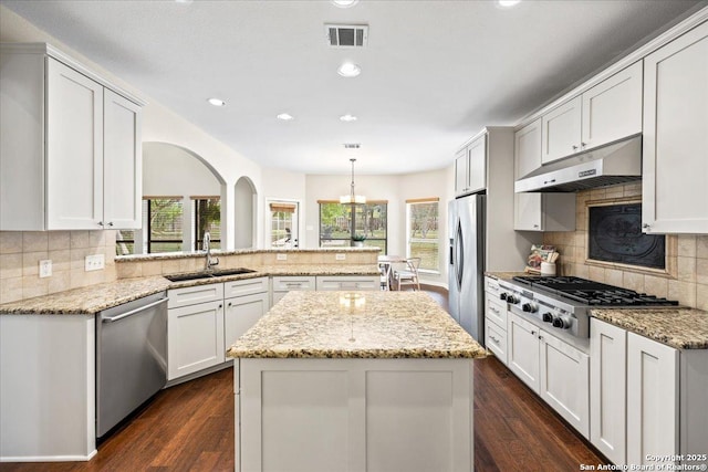 kitchen featuring a peninsula, a sink, visible vents, under cabinet range hood, and appliances with stainless steel finishes