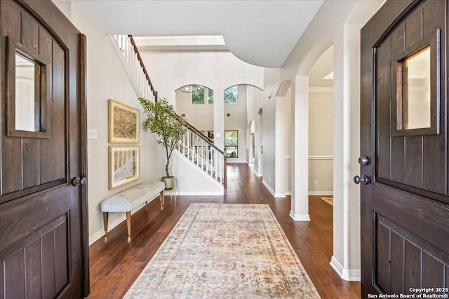 foyer entrance with baseboards, arched walkways, stairs, and dark wood-style flooring