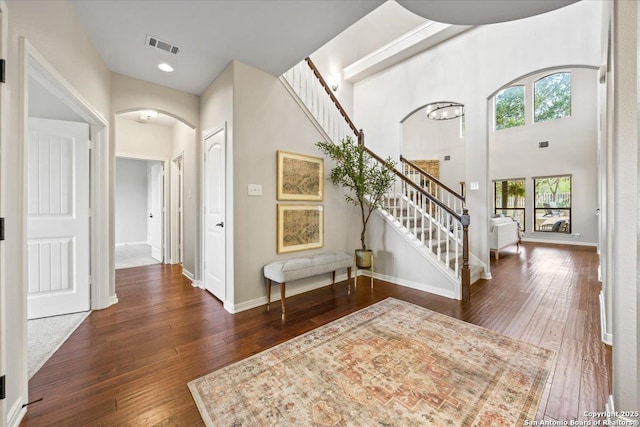 foyer with arched walkways, baseboards, visible vents, stairway, and hardwood / wood-style floors