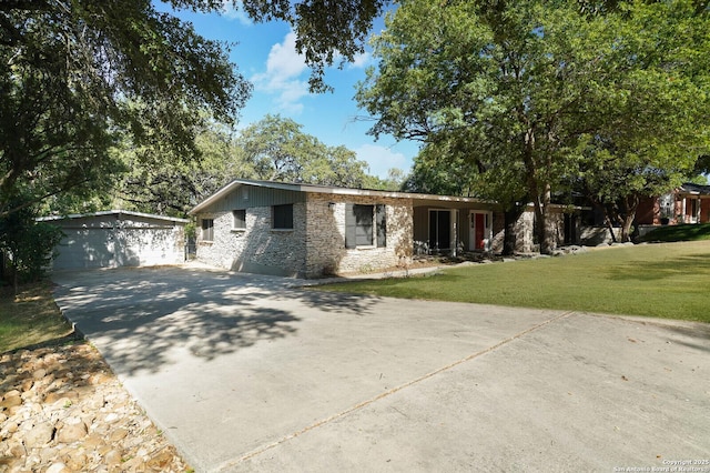 view of front of house featuring concrete driveway, an outbuilding, stone siding, a front yard, and a garage