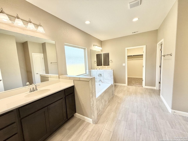 full bathroom with a spacious closet, wood finished floors, visible vents, a sink, and a garden tub