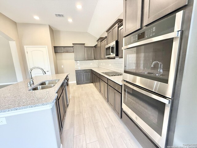 kitchen with stainless steel appliances, a sink, visible vents, decorative backsplash, and light stone counters