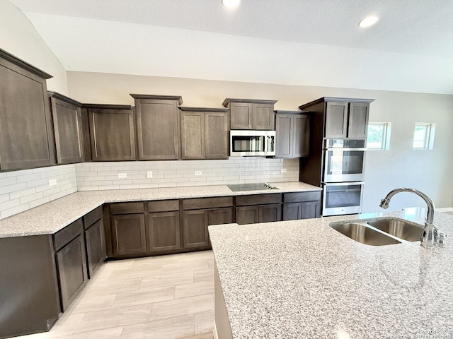 kitchen with backsplash, appliances with stainless steel finishes, dark brown cabinetry, and a sink