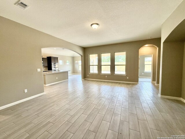 unfurnished living room with arched walkways, light wood-style floors, and visible vents