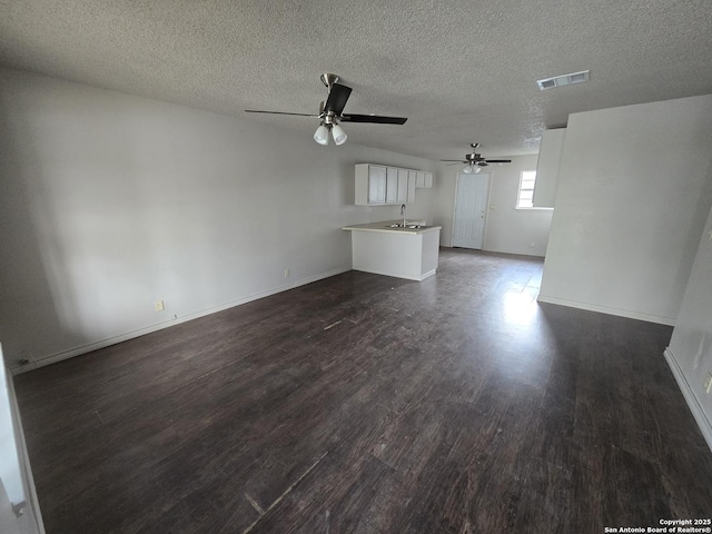 unfurnished living room featuring a sink, ceiling fan, visible vents, baseboards, and dark wood finished floors