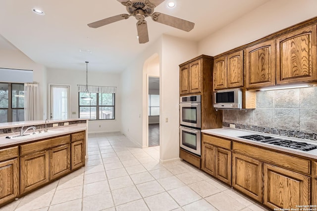 kitchen featuring decorative backsplash, brown cabinetry, gas stovetop, light tile patterned floors, and double oven