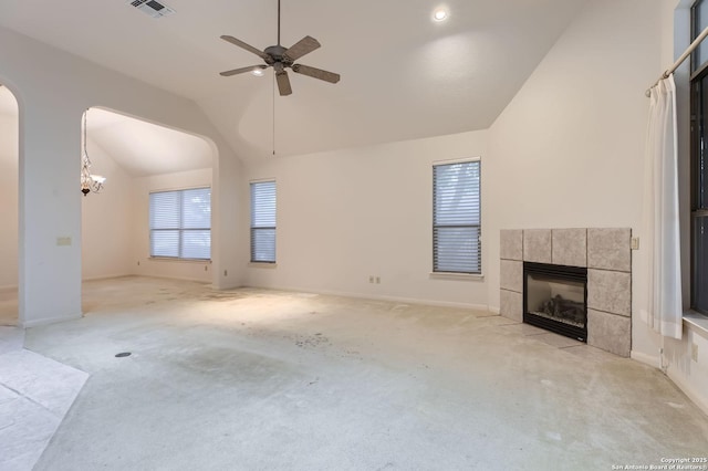 unfurnished living room with lofted ceiling, a tile fireplace, a ceiling fan, light carpet, and arched walkways