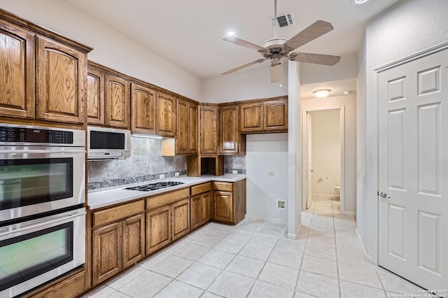 kitchen featuring brown cabinets, light tile patterned floors, double oven, white microwave, and backsplash