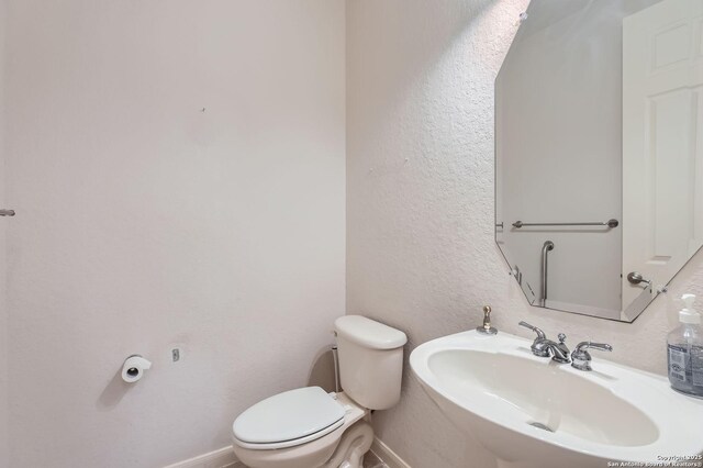 half bathroom with a textured wall, toilet, baseboards, and a sink