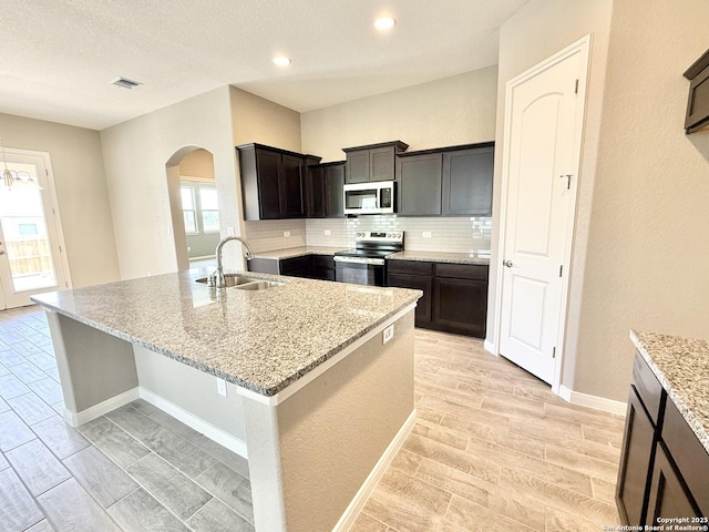 kitchen featuring a sink, wood tiled floor, arched walkways, stainless steel appliances, and backsplash