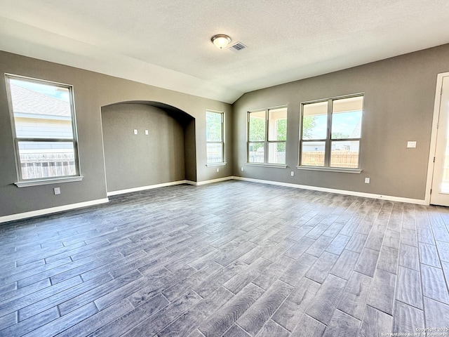 spare room featuring wood finished floors, a textured ceiling, arched walkways, baseboards, and visible vents