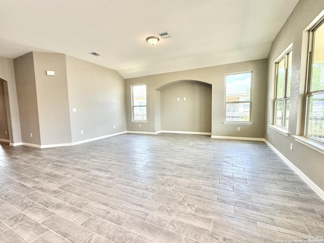 spare room with light wood-type flooring, baseboards, visible vents, and arched walkways