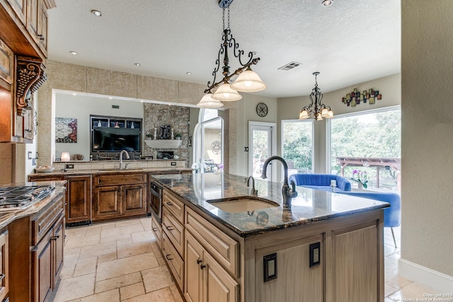 kitchen with a sink, dark stone countertops, a textured ceiling, a center island with sink, and visible vents