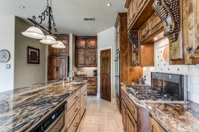kitchen with dark stone counters, a sink, stainless steel gas cooktop, stone tile flooring, and visible vents