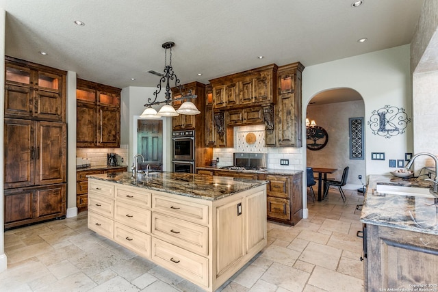 kitchen with stainless steel double oven, decorative backsplash, arched walkways, and a sink