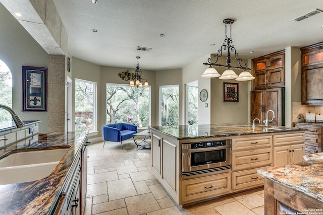 kitchen featuring a wealth of natural light, oven, stone tile floors, and a sink