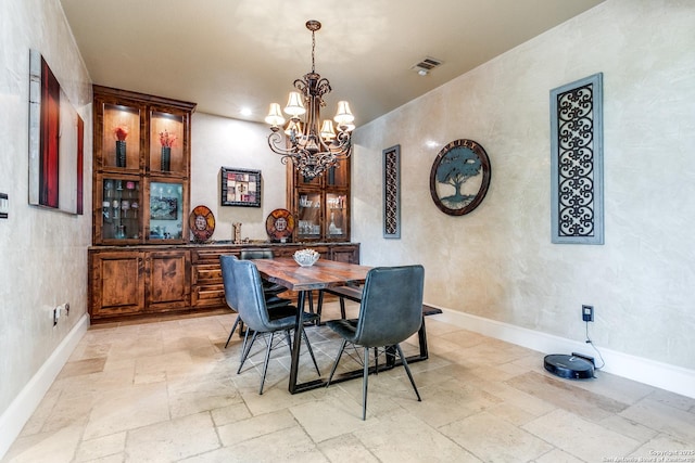 dining room with stone tile flooring, visible vents, baseboards, and a notable chandelier