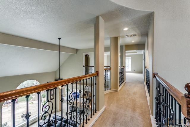 corridor featuring a textured ceiling, beamed ceiling, baseboards, carpet flooring, and visible vents