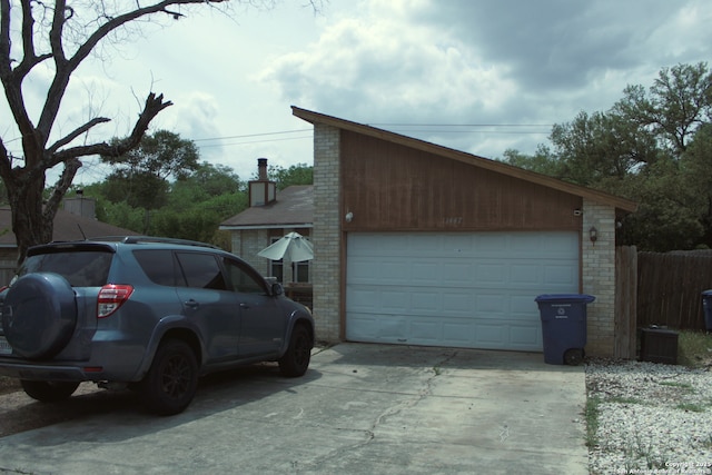 view of side of property featuring driveway, fence, brick siding, and a garage