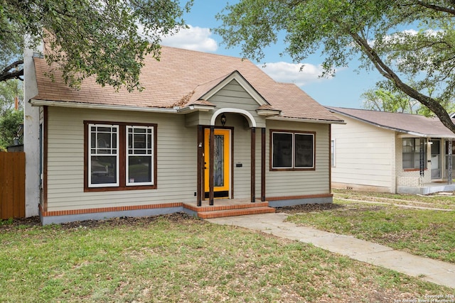 bungalow-style house with roof with shingles, a front lawn, and fence