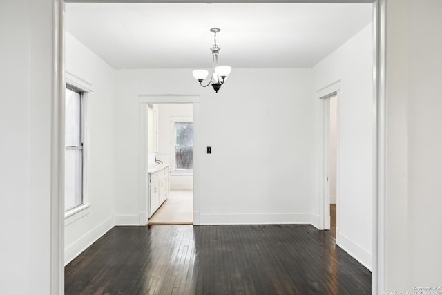 unfurnished dining area with dark wood finished floors, baseboards, and a notable chandelier