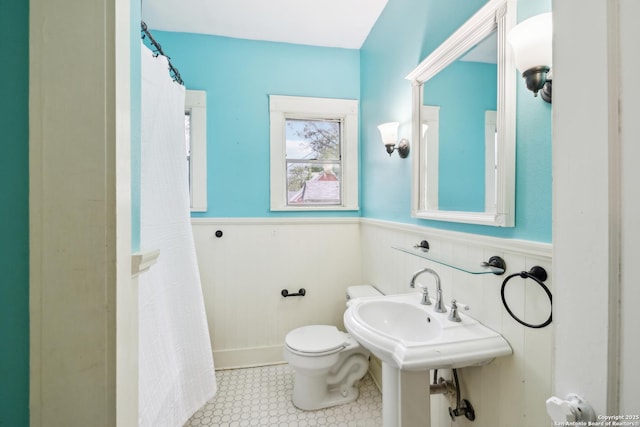 bathroom featuring a shower with shower curtain, toilet, and a wainscoted wall