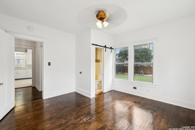 unfurnished room with hardwood / wood-style flooring, baseboards, a ceiling fan, and a barn door
