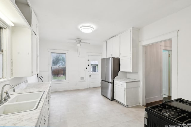 kitchen with a sink, gas range, light countertops, white cabinets, and freestanding refrigerator