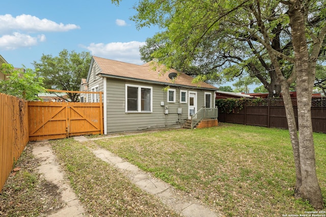 back of house featuring a gate, a fenced backyard, and a lawn