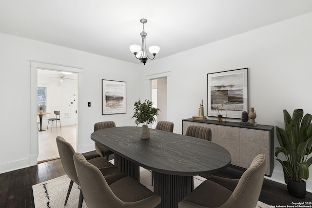 dining room with ceiling fan with notable chandelier, baseboards, and dark wood-style floors