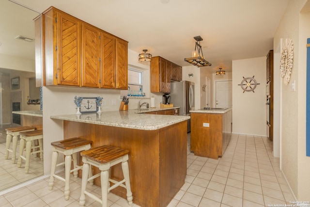 kitchen featuring a peninsula, brown cabinetry, a sink, and light tile patterned floors