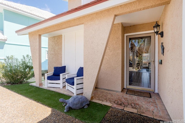 view of exterior entry featuring stucco siding and a patio area