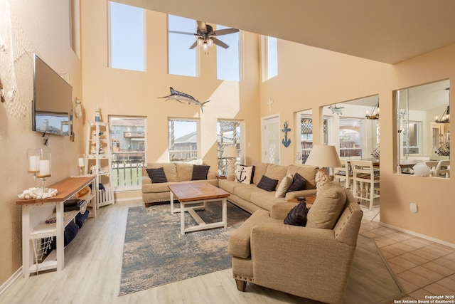 living area featuring wood finished floors, a high ceiling, baseboards, and ceiling fan with notable chandelier