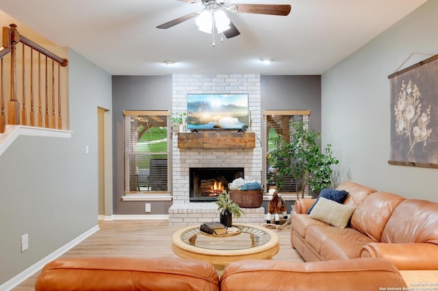 living area featuring ceiling fan, baseboards, a brick fireplace, and wood finished floors