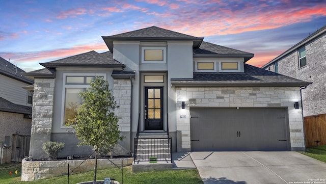 view of front facade with driveway, stone siding, a shingled roof, an attached garage, and fence