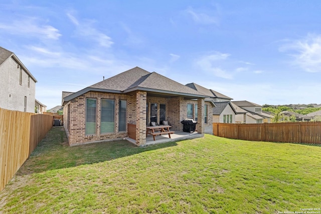 rear view of house with a patio area, a shingled roof, a fenced backyard, a yard, and brick siding