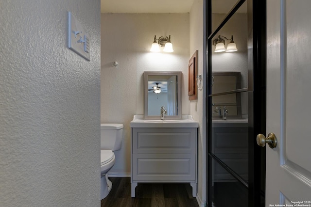 bathroom featuring wood finished floors, toilet, vanity, and a textured wall