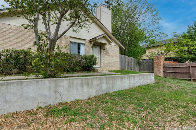 exterior space with a chimney, brick siding, fence, and a lawn