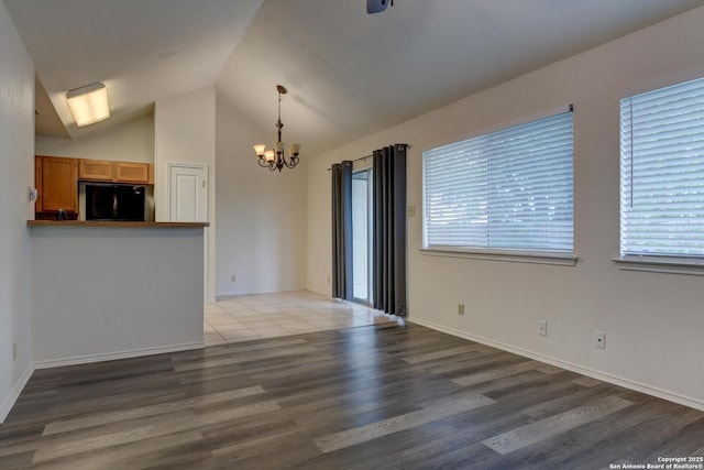 unfurnished living room featuring lofted ceiling, baseboards, wood finished floors, and a notable chandelier