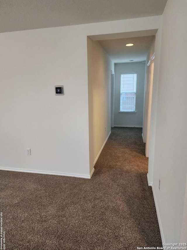 hallway featuring dark colored carpet and baseboards