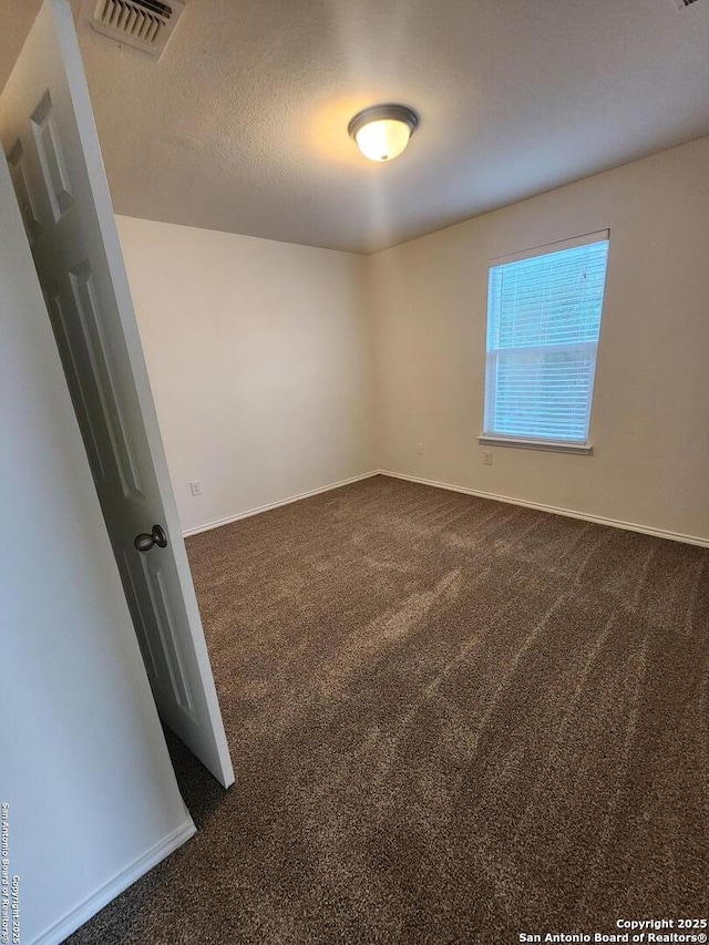 spare room featuring dark carpet, visible vents, and baseboards