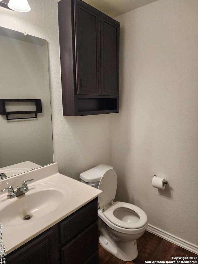 half bathroom featuring toilet, vanity, wood finished floors, and baseboards