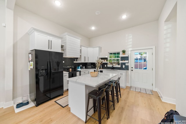 kitchen featuring black appliances, white cabinetry, a breakfast bar area, and light wood-style flooring