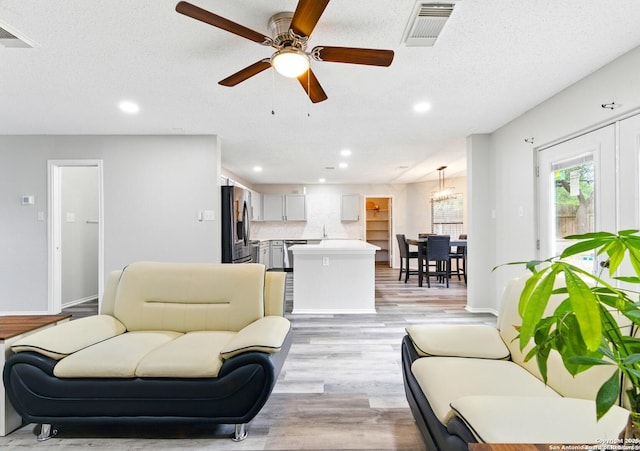 living room featuring light wood finished floors, ceiling fan with notable chandelier, visible vents, and recessed lighting