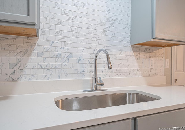 details featuring tasteful backsplash, light stone countertops, and a sink